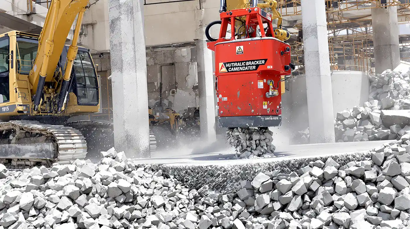 Excavator with hydraulic breaker attachment breaking up a thick concrete slab with exposed rebar on a Kansas City commercial demolition site