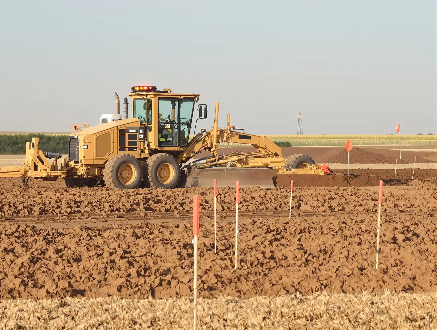 Caterpillar motor grader with laser-guided controls shaping a commercial building pad in Kansas City