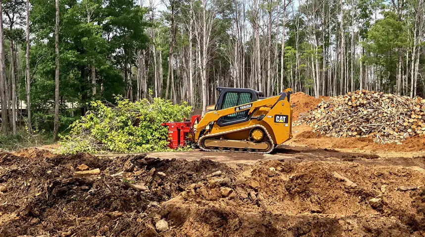 Tracked skid steer pushing brush on a large land clearing operation in Kansas City with raw brown dirt and piles of cut wood