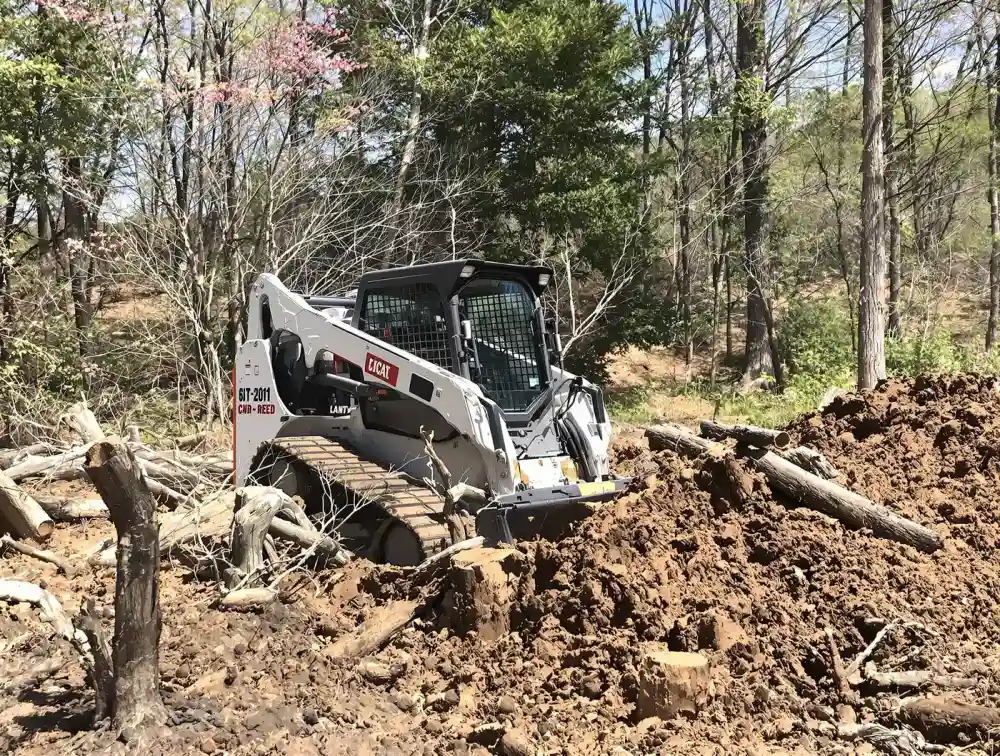 Tracked skid steer clearing brush and stumps on a partially cleared Kansas City suburban lot